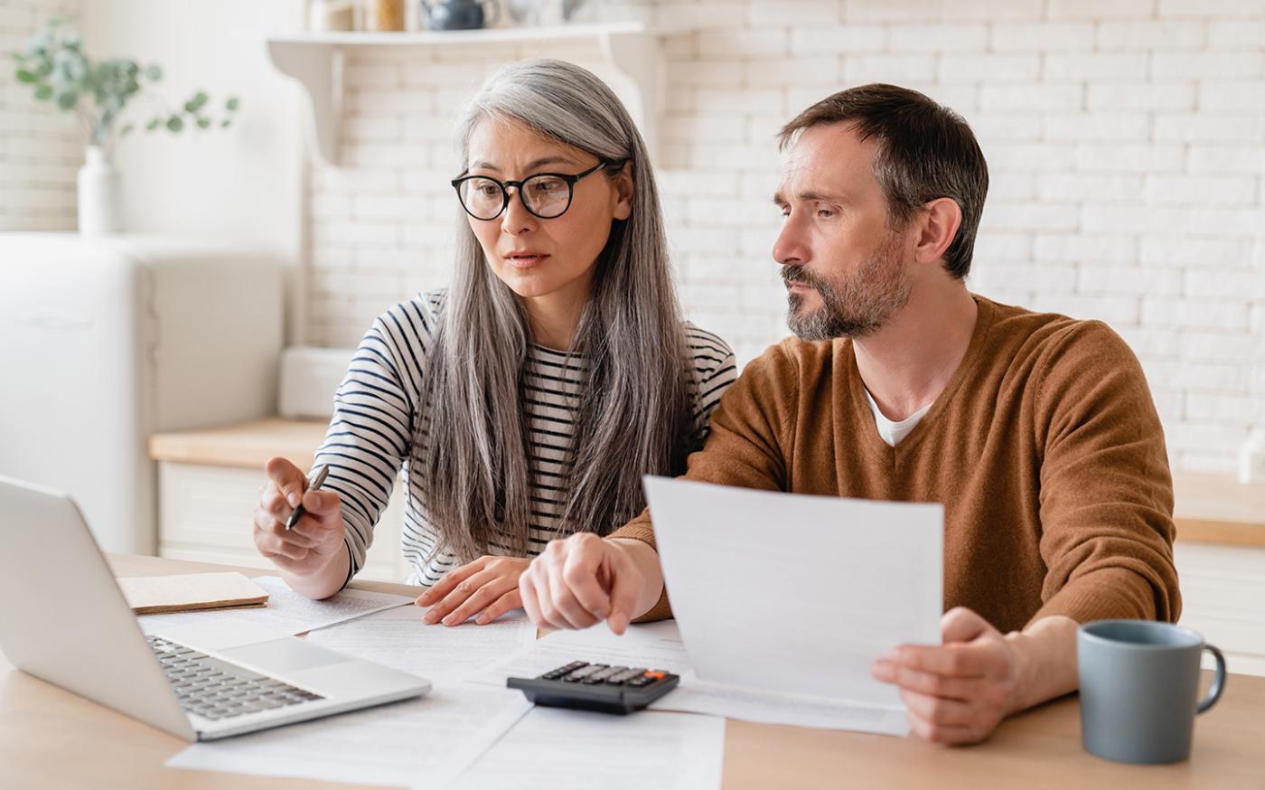 middle aged couple looking over documents on laptop